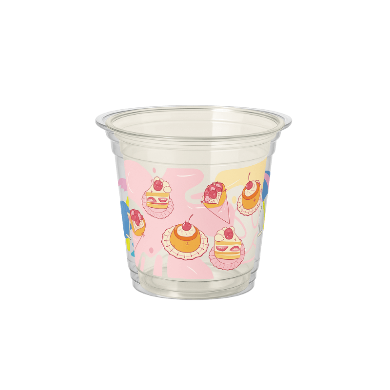 Clear plastic cup with a pastel dessert pattern (cakes and cherries) on a pink abstract background, shown on a white background.