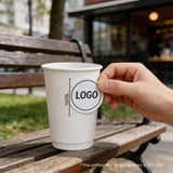 16oz double wall white paper cup with logo sticker displayed on a café tabletop.