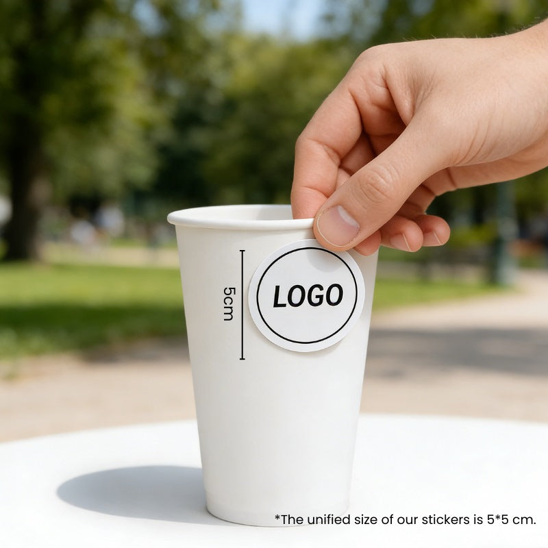 Applying a logo sticker to a large 16oz single wall white paper cup in a café setting.