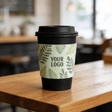 Black takeaway cup wrapped with a green leaf-pattern cup sleeve featuring a customizable logo on a cafe table.