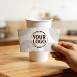 Hand holding a white cup sleeve with minimalist line patterns and a customizable logo in front of a white paper cup.