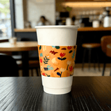 White paper cup wrapped with an orange floral-pattern cup sleeve on a cafe table.