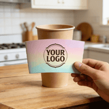 Hand holding a customizable logo cup sleeve with a soft pastel gradient design in front of a kraft paper cup.