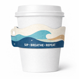 White paper cup with a wavy, ocean-themed sleeve in blues and beige reading “SIP • BREATHE • REPEAT.
